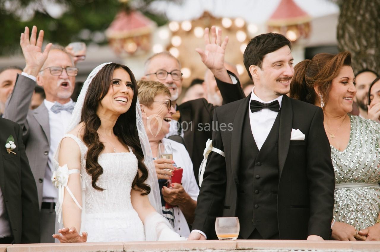 Un couple de mariés souriants entouré d'invités célébrant en plein air.