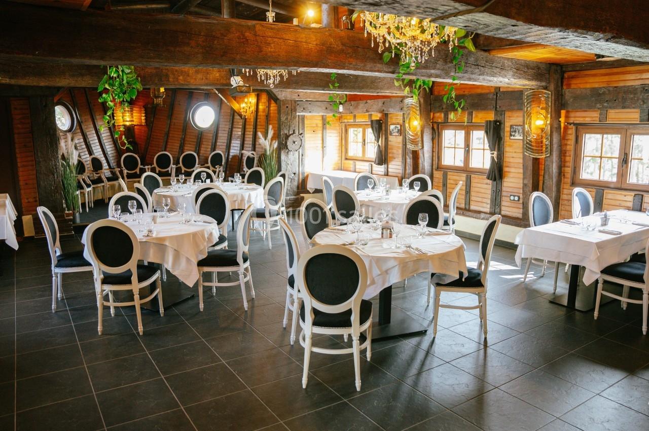 Salle de restaurant lumineuse avec tables dressées, chaises élégantes et poutres apparentes en bois.
