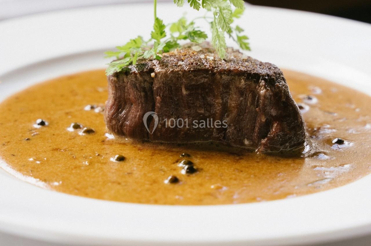 Pièce de viande servie avec une sauce au poivre, garnie de persil, présentée dans une assiette blanche.