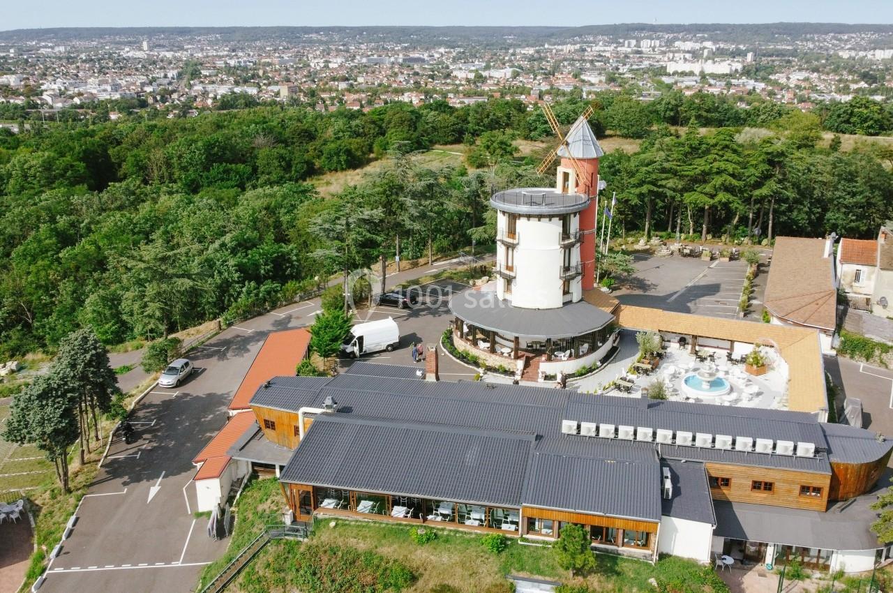 Vue aérienne d'un complexe avec un moulin rénové, une piscine et des bâtiments modernes entourés de verdure.