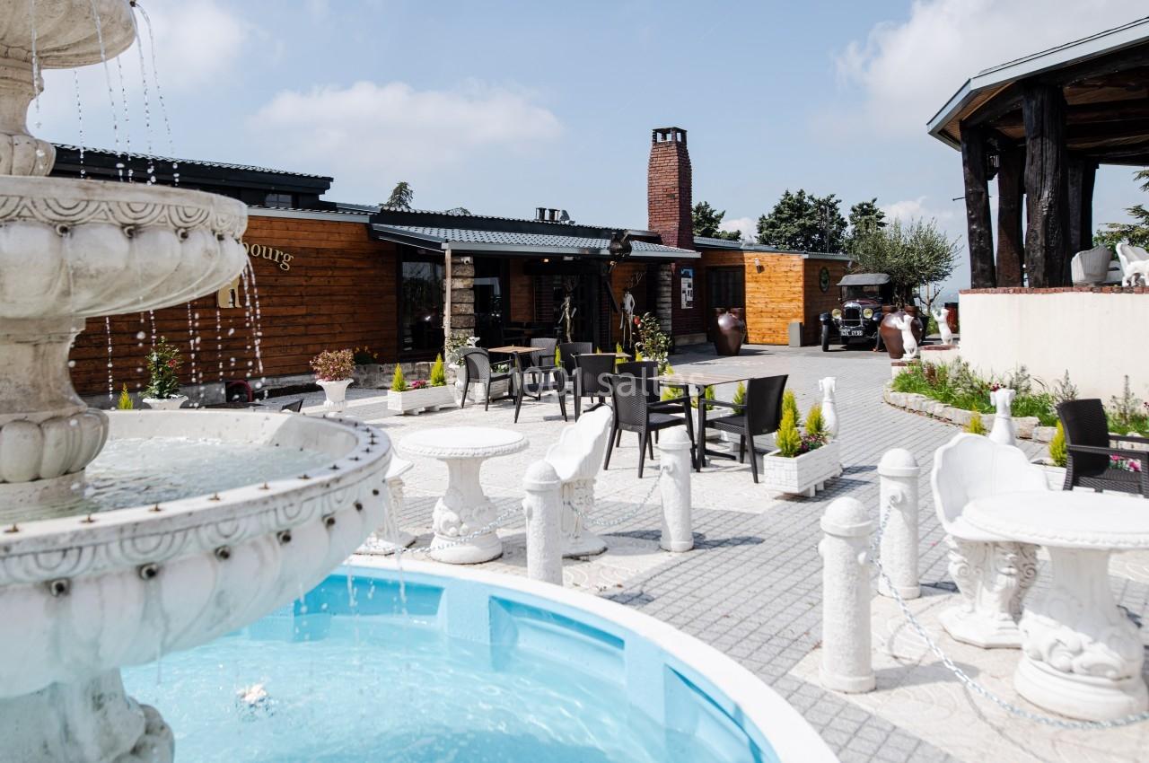Cour extérieure avec une fontaine en premier plan, entourée de tables et chaises, devant un bâtiment en bois.