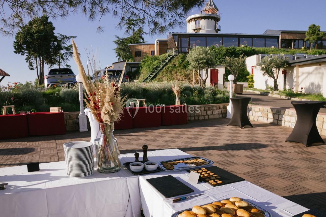 Table dressée en extérieur avec viennoiseries, assiettes et décorations florales, devant un bâtiment moderne.
