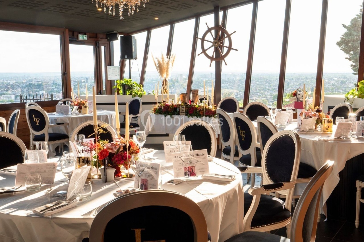 Salle de réception élégante avec tables rondes dressées, grandes baies vitrées offrant une vue panoramique sur la ville.