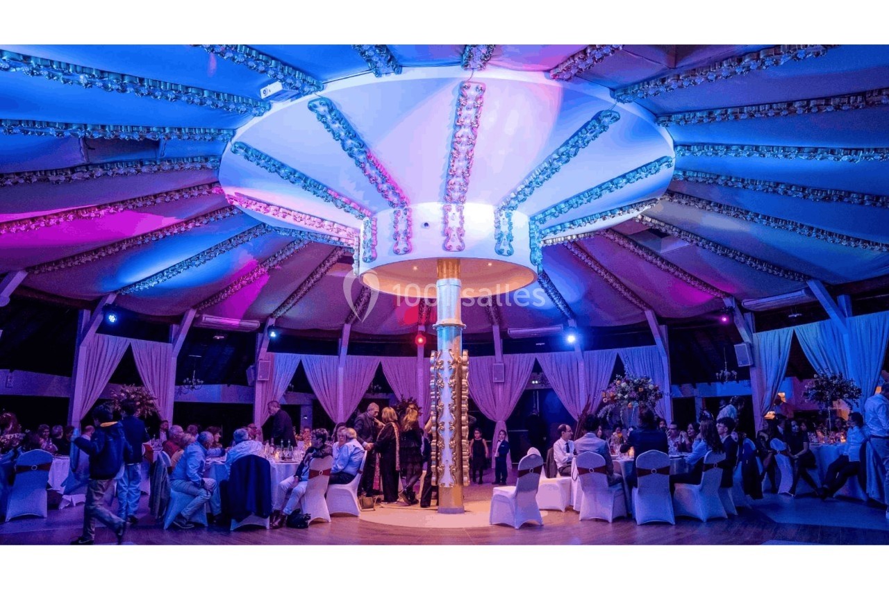 Salle de réception décorée avec des lumières colorées, des tables dressées et des invités assis lors d'un événement.
