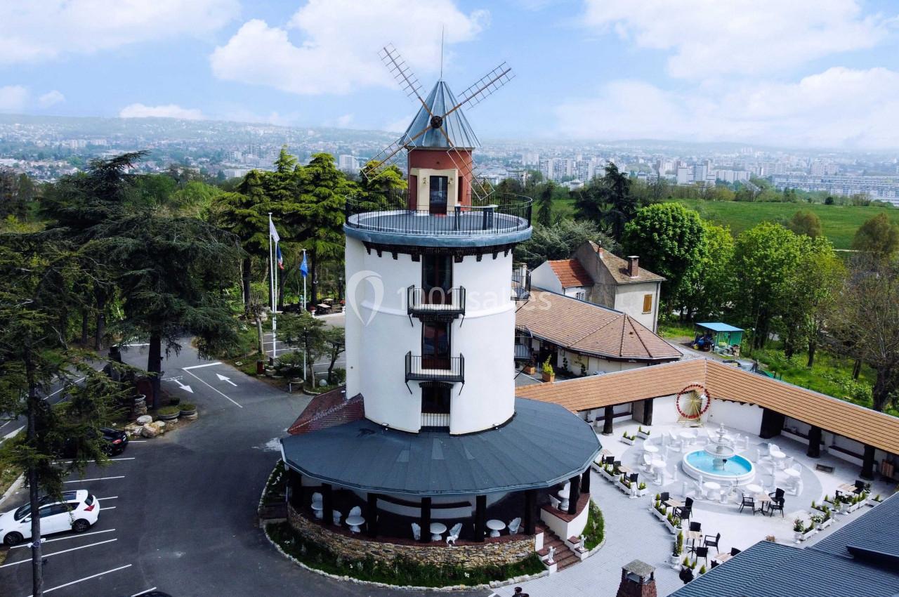 Vue aérienne d'un bâtiment en forme de moulin entouré de verdure, avec une cour centrale et une piscine.