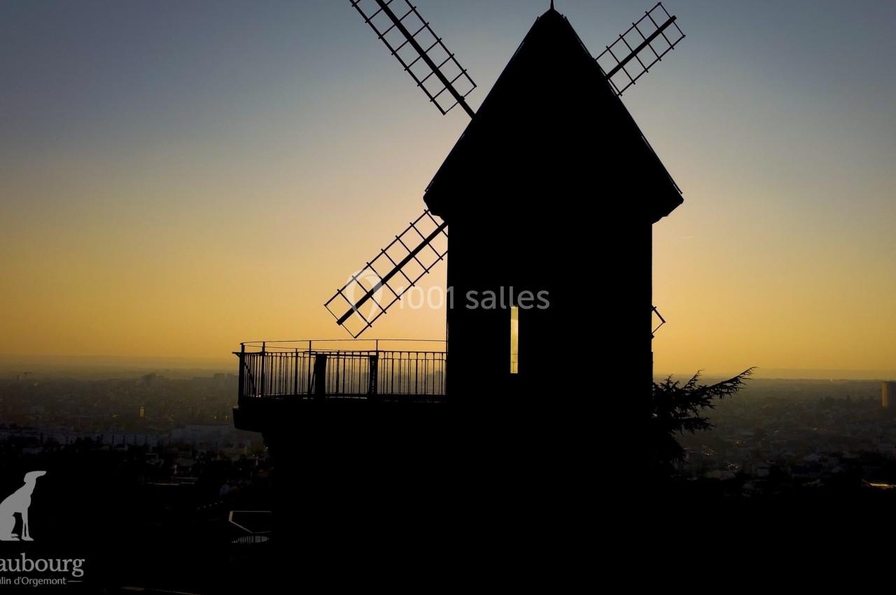 Silhouette d'un moulin à vent au coucher du soleil, avec une vue dégagée sur une ville en arrière-plan.