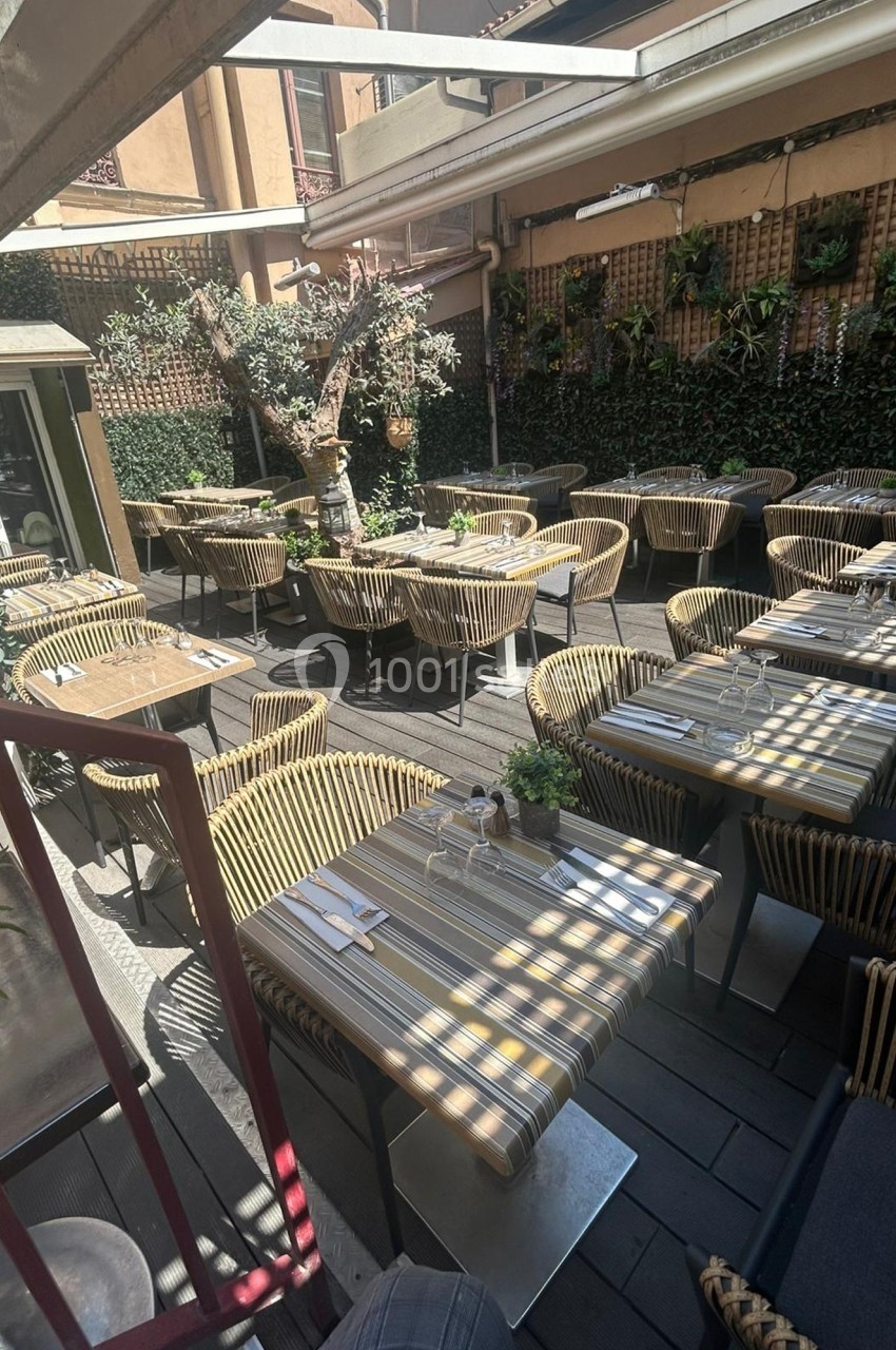 Terrasse d'un restaurant avec des tables dressées, des chaises en rotin et des plantes grimpantes sur les murs.