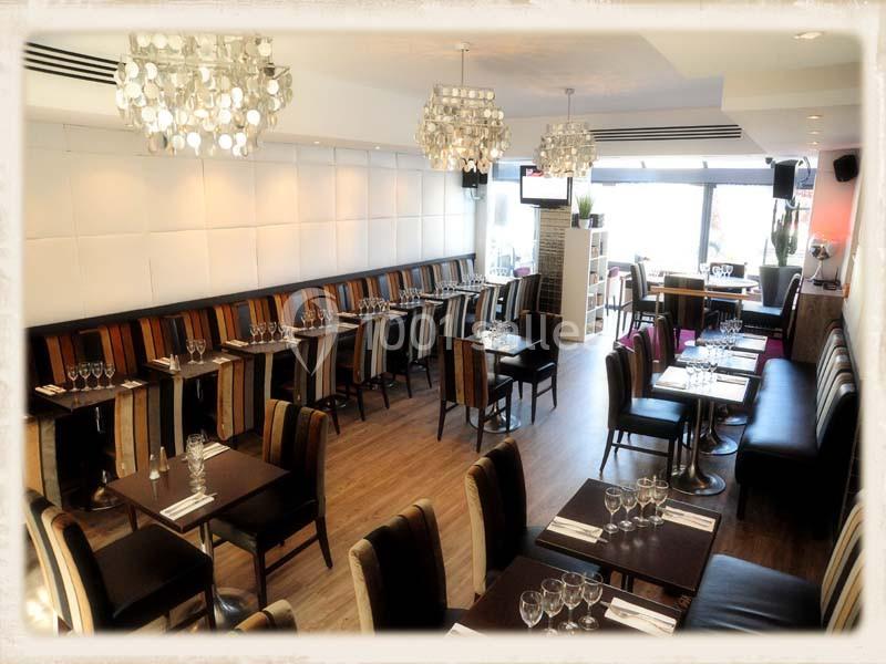 Salle de restaurant lumineuse avec tables alignées, chaises colorées et lustres modernes.