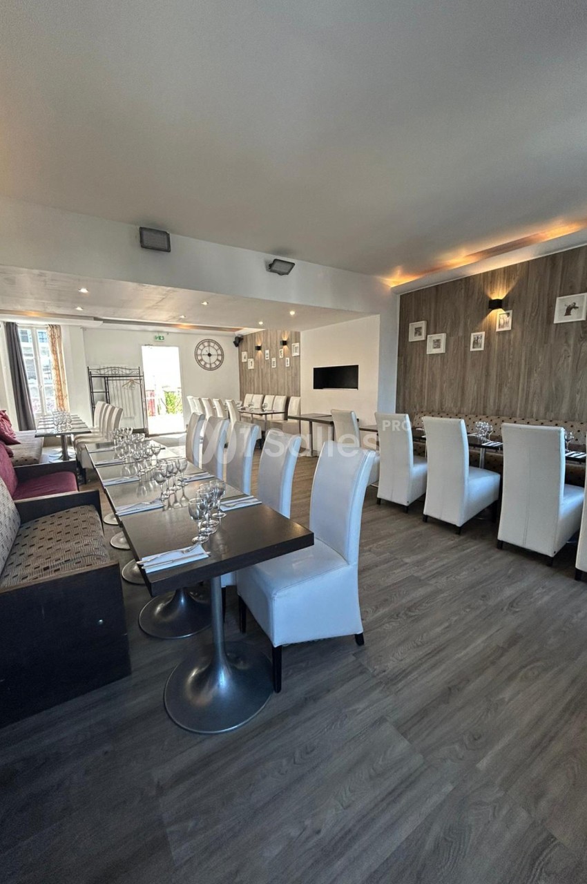 Salle de restaurant lumineuse avec tables dressées, chaises blanches et banquettes, décor moderne et épuré.