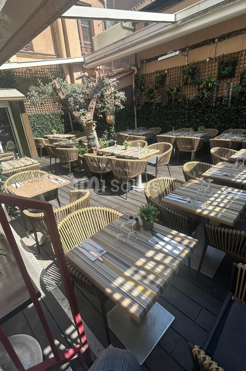 Terrasse d'un restaurant avec des tables dressées, des chaises en rotin et des plantes grimpantes sur les murs.