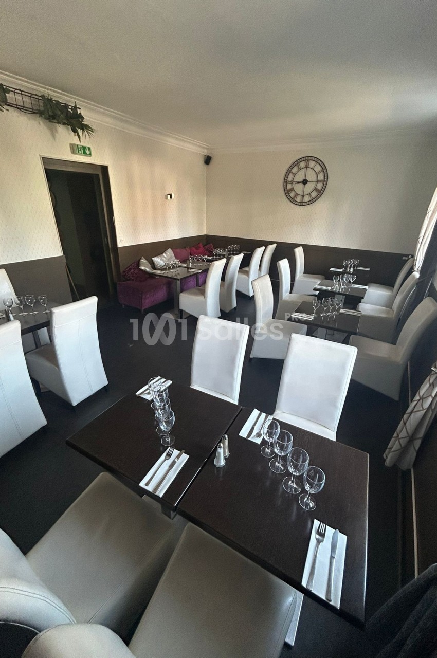 Salle de restaurant avec tables dressées, chaises blanches et décoration sobre, éclairée par la lumière naturelle.