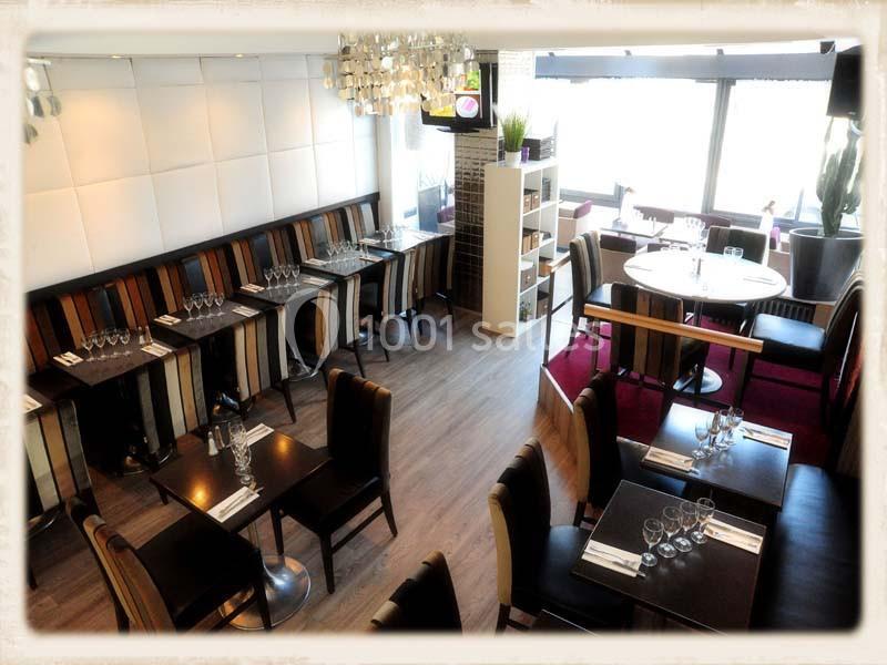 Salle de restaurant lumineuse avec tables dressées, chaises colorées et grandes baies vitrées.