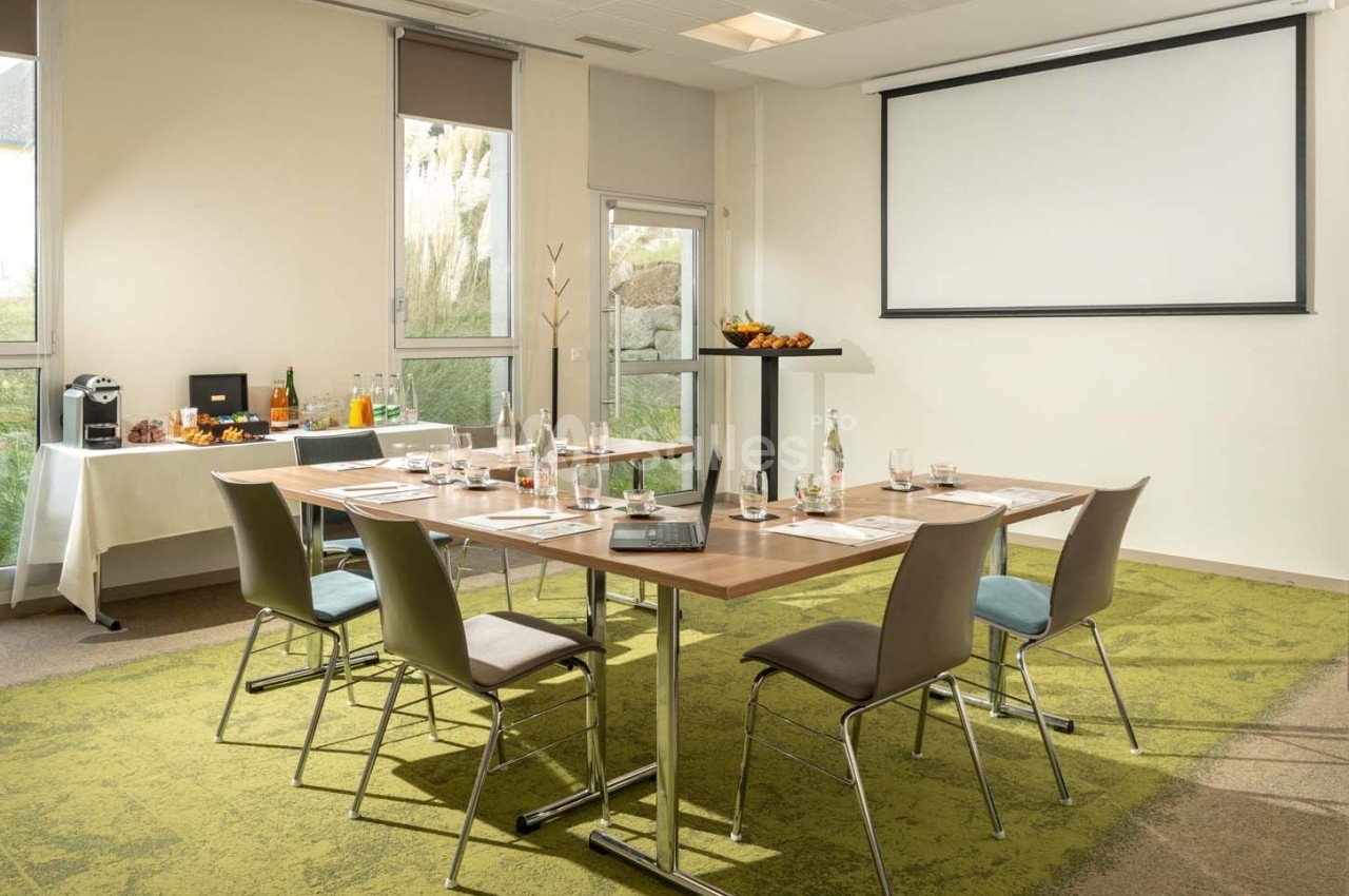 Salle de réunion lumineuse avec table équipée de documents, boissons et écran de projection en arrière-plan.