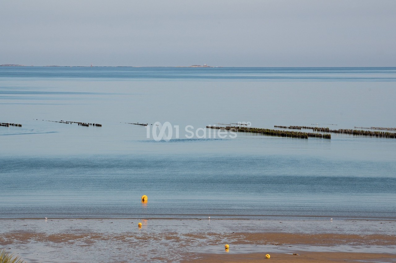 Vue d'une plage à marée basse avec des bouées jaunes et des structures ostréicoles dans une mer calme.