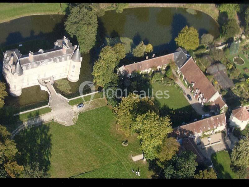 Vue aérienne d'un château entouré d'un parc verdoyant, avec des bâtiments annexes et un plan d'eau adjacent.