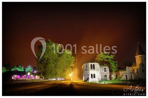 Ruines éclairées d'un bâtiment historique entouré d'arbres, sous un ciel nocturne orangé.