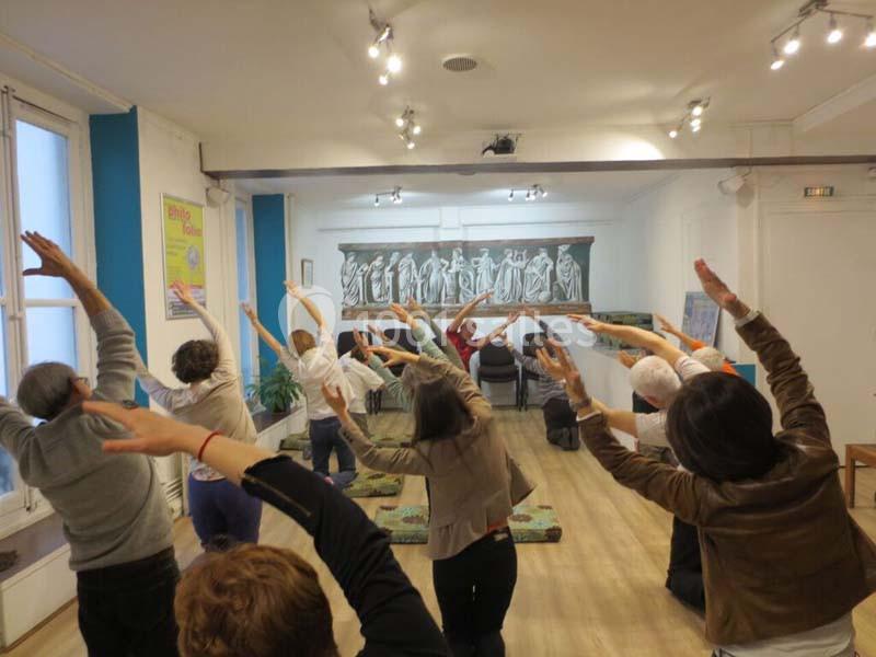 Personnes effectuant des exercices d'étirement en groupe dans une salle lumineuse avec un tableau en arrière-plan.