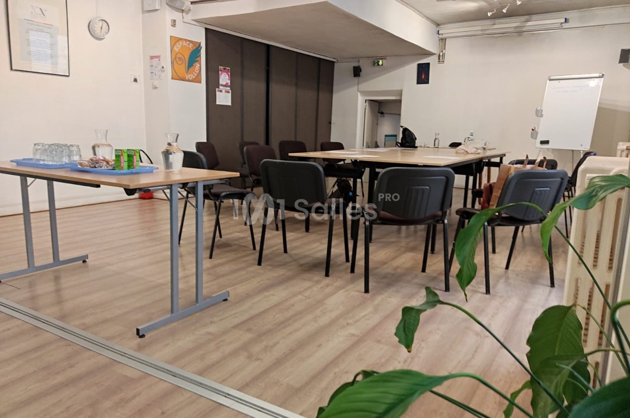 Salle de réunion avec des chaises disposées autour de tables, un tableau blanc et des boissons sur une table latérale.