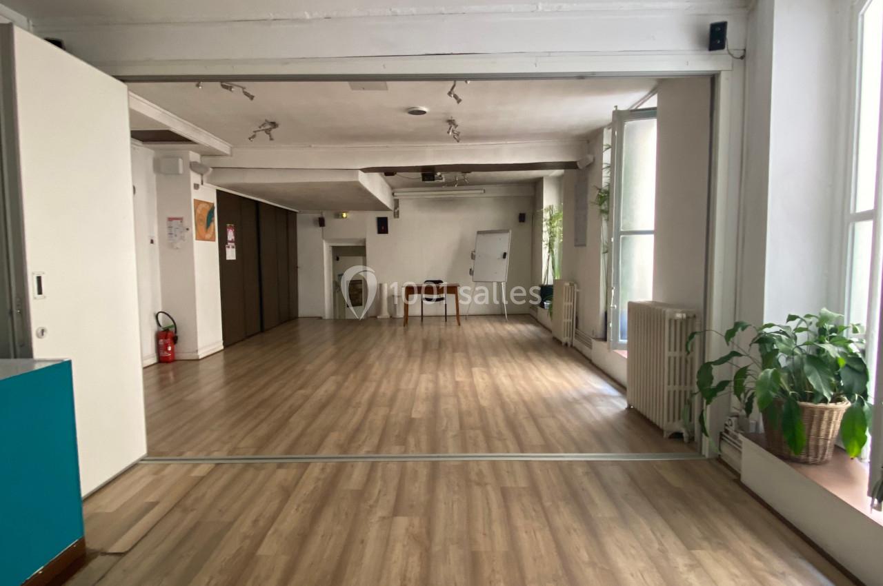 Salle lumineuse avec parquet clair, murs blancs, grandes fenêtres, plantes en pot et mobilier minimaliste.