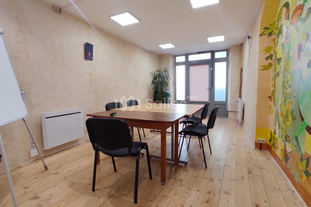 Salle de réunion lumineuse avec table en bois, chaises noires, tableau blanc, plante et fresque murale colorée.