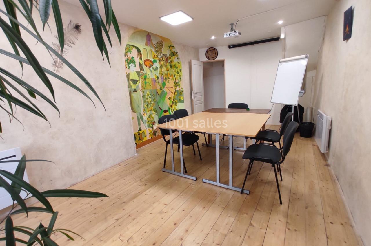 Salle de réunion lumineuse avec table en bois, chaises noires, tableau blanc, projecteur et mur décoré d'une fresque colorée.