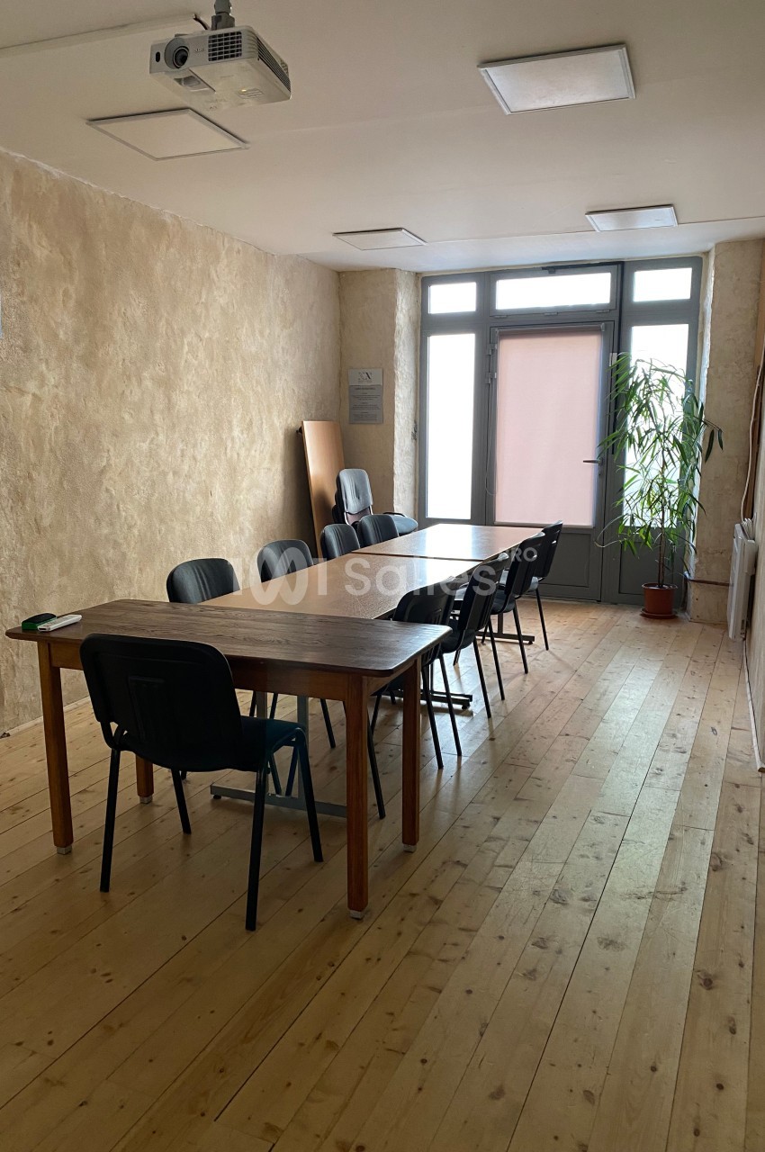 Salle de réunion avec une grande table en bois, plusieurs chaises noires et une plante près d'une fenêtre.