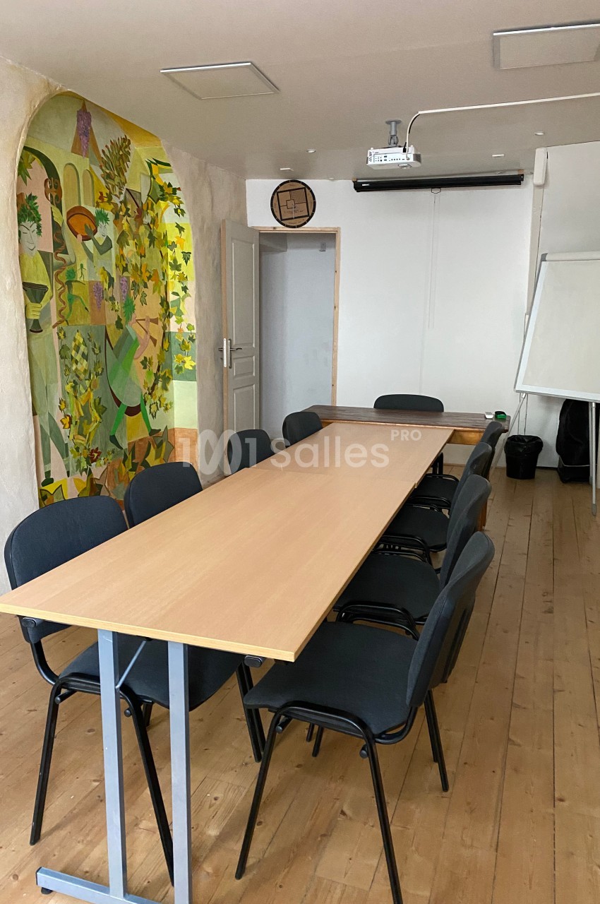Salle de réunion avec une longue table en bois, des chaises noires, un tableau blanc et une fresque colorée sur le mur.
