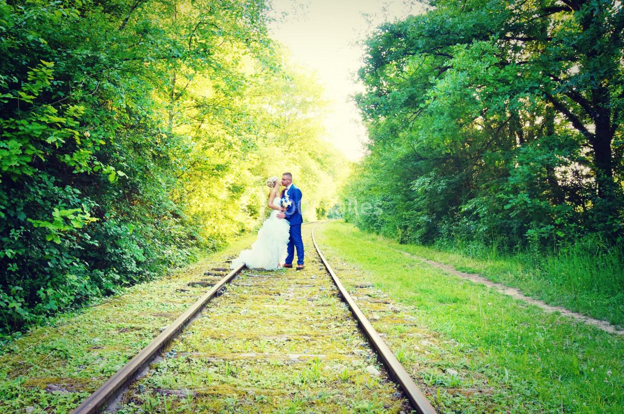 Un couple en tenue de mariage pose sur des rails entourés de végétation verdoyante.