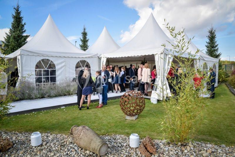 Personnes rassemblées sous des tentes blanches dans un jardin, lors d'un événement en plein air par temps clair.