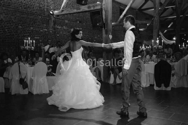 Un couple en tenue de mariage danse dans une salle décorée, entouré d'invités assis à des tables.