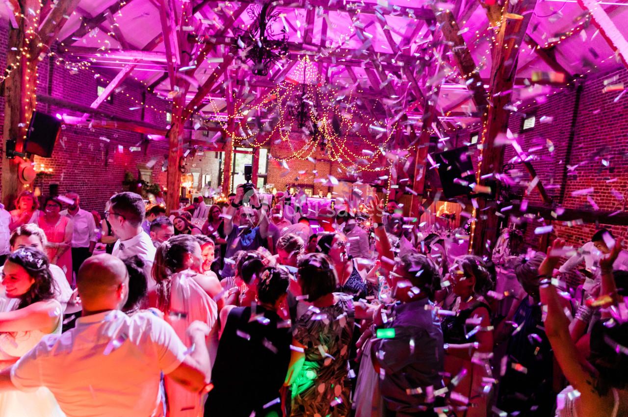 Groupe de personnes dansant sous des lumières colorées et des guirlandes dans une salle en bois décorée.