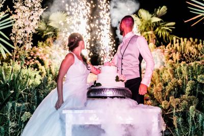 Un couple en tenue de mariage se tient la main dans un jardin baigné par une lumière douce au coucher du soleil.