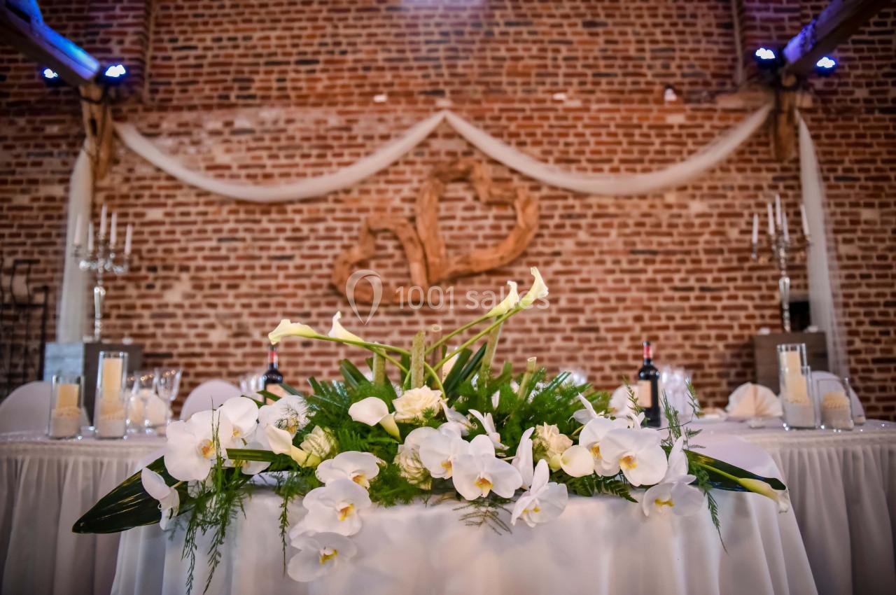 Décoration florale blanche sur une table de réception devant un mur en briques avec des ornements en bois.