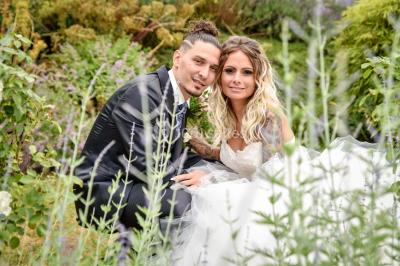 Un couple en tenue de mariage se tient la main dans un jardin baigné par une lumière douce au coucher du soleil.