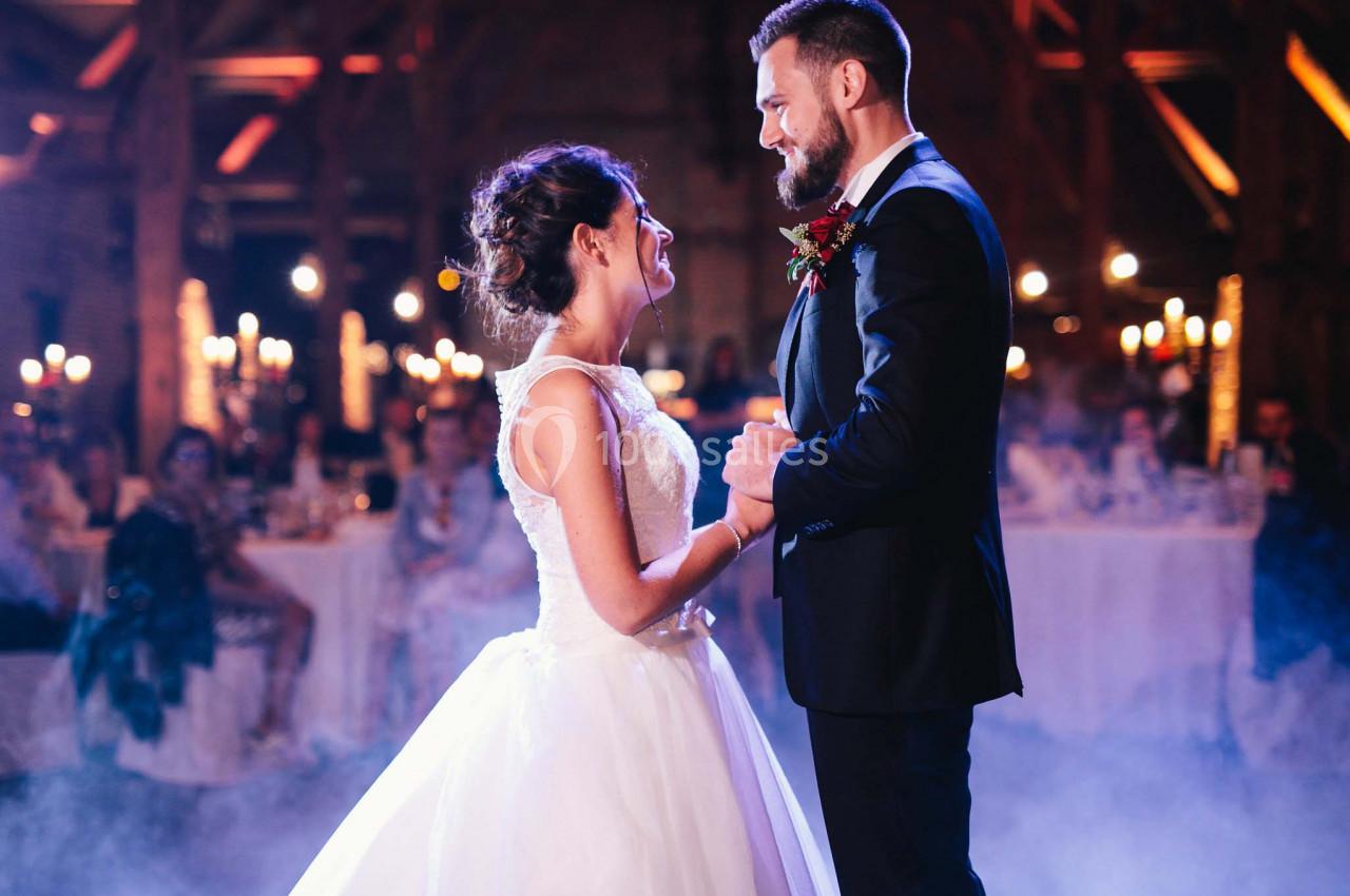 Un couple en tenue de mariage danse dans une salle éclairée par des lumières tamisées et des bougies.