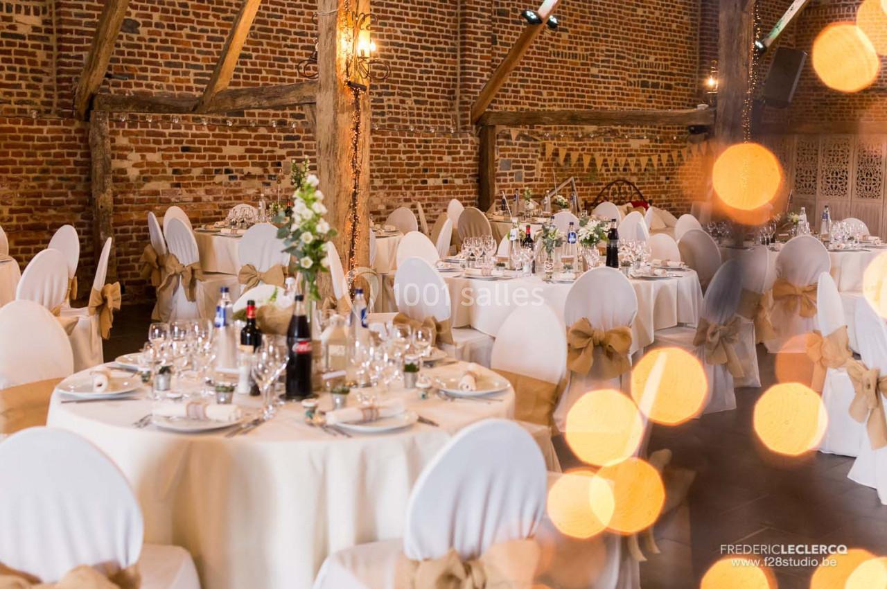 Salle de réception décorée avec des tables rondes dressées, nappes blanches et chaises ornées de nœuds beige.