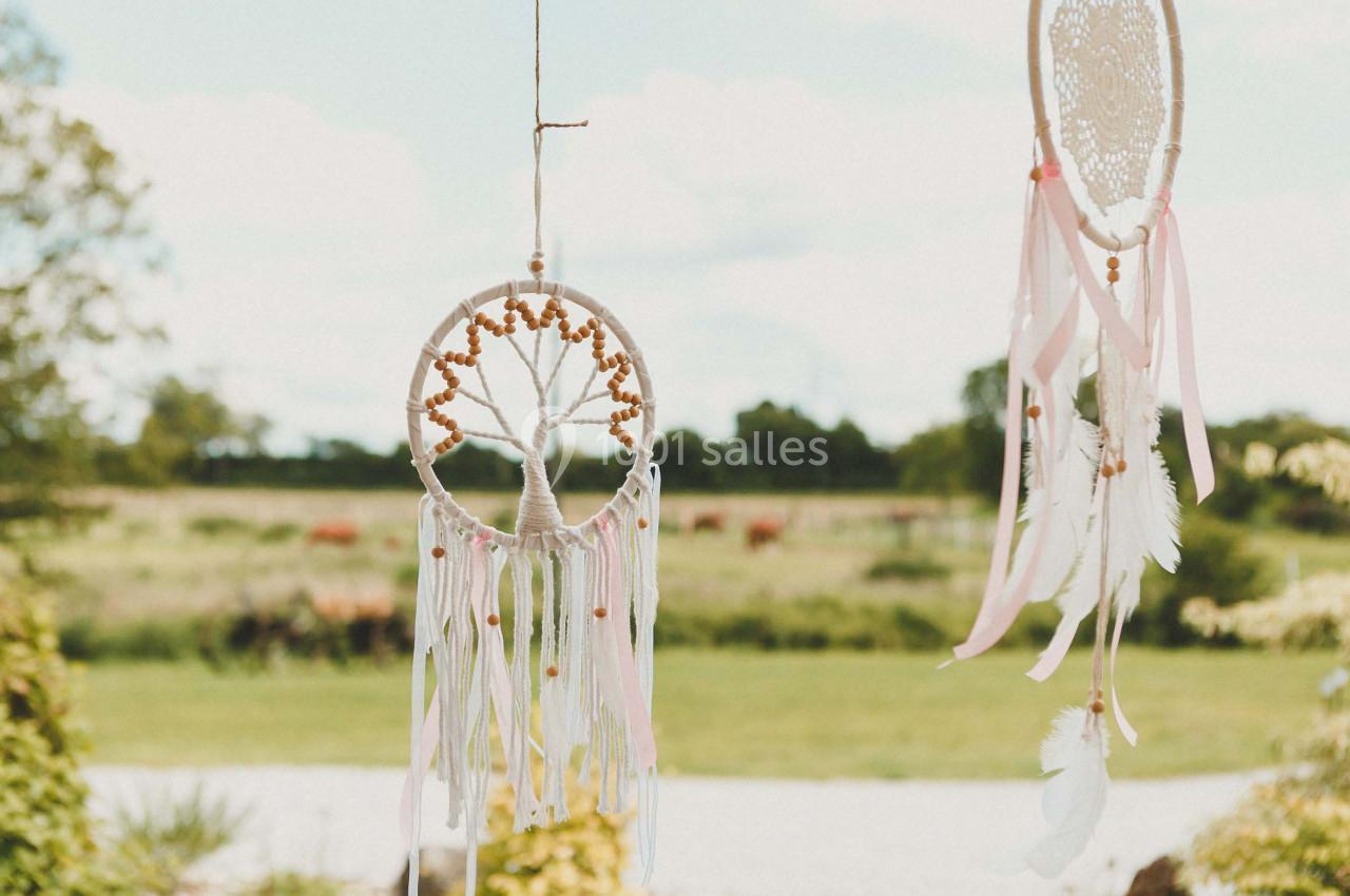Deux attrape-rêves ornés de plumes et rubans suspendus en extérieur avec un paysage champêtre en arrière-plan.