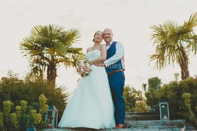 Un couple en tenue de mariage se tient la main dans un jardin baigné par une lumière douce au coucher du soleil.