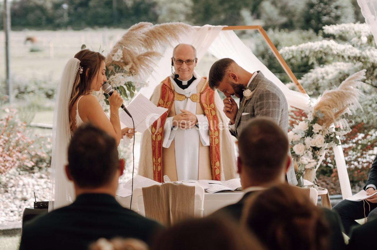 Une mariée lit un discours émouvant devant un marié ému, un prêtre et des invités lors d'une cérémonie en plein air.