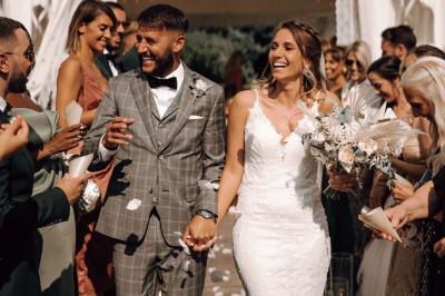 Un couple en tenue de mariage se tient la main dans un jardin baigné par une lumière douce au coucher du soleil.