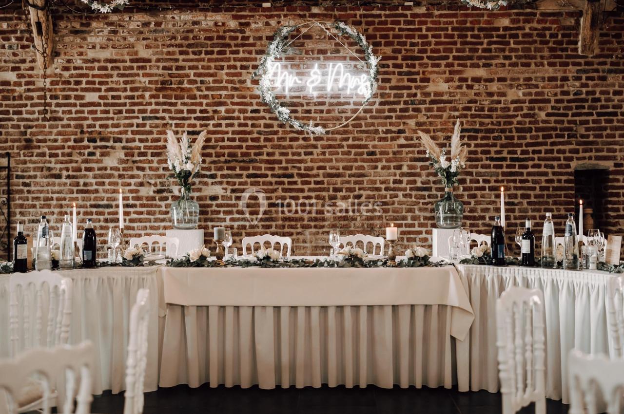 Table de réception élégamment décorée avec nappes blanches, bougies, fleurs et mur de briques en arrière-plan.