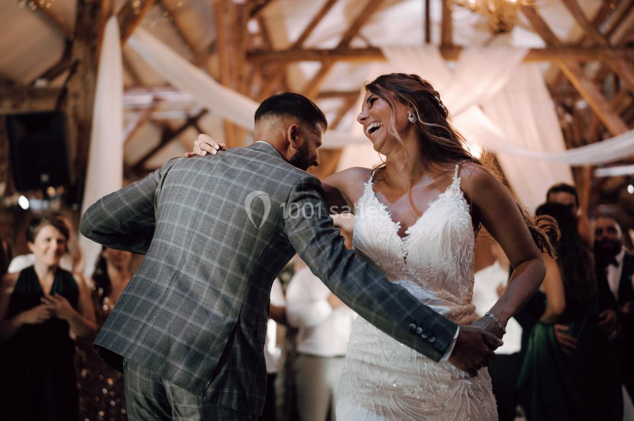 Un couple en tenue de mariage danse joyeusement dans une salle décorée de bois et de drapés blancs.