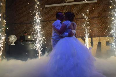 Un couple en tenue de mariage se tient la main dans un jardin baigné par une lumière douce au coucher du soleil.