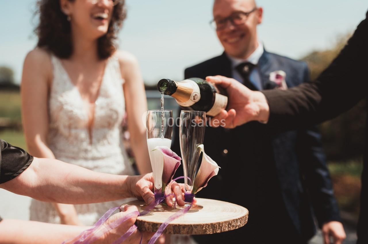 Deux flûtes de champagne sont remplies sur un plateau en bois lors d'une cérémonie en extérieur.