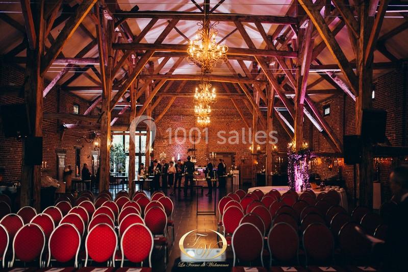 Salle de réception en briques avec poutres apparentes, rangées de chaises rouges et éclairage chaleureux.