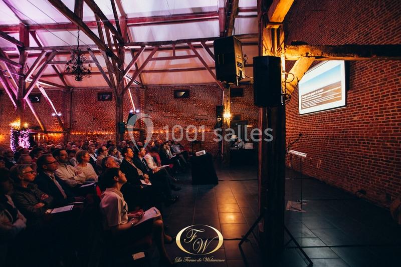 Salle en briques avec un public assis, regardant une présentation projetée sur un écran.