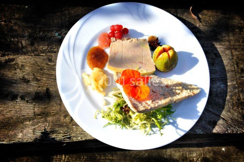 Assiette contenant du foie gras, figue, groseilles, confiture, salade verte et pain sur une table en bois rustique.