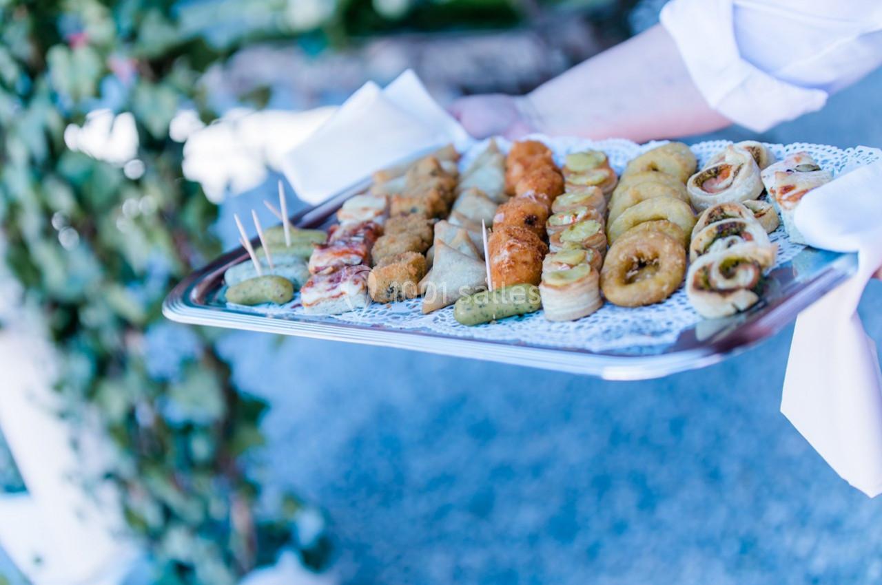Plateau de bouchées apéritives variées présentées sur un napperon blanc, tenu par une personne en chemise blanche.