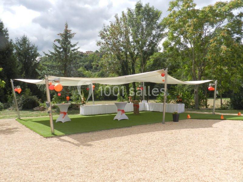 Espace extérieur aménagé avec tonnelle blanche, tables décorées et ballons rouges, entouré de verdure.