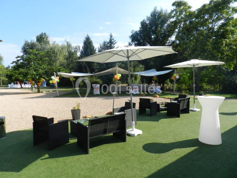 Mobilier de jardin noir avec parasols blancs sur une pelouse artificielle, entouré d'arbres et de décorations festives.
